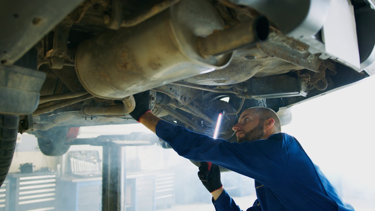 Skilled mechanic performing thorough maintenance under a vehicle in a professional garage setting.