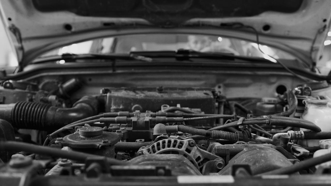 Detailed black and white close-up of a car engine bay with visible components.